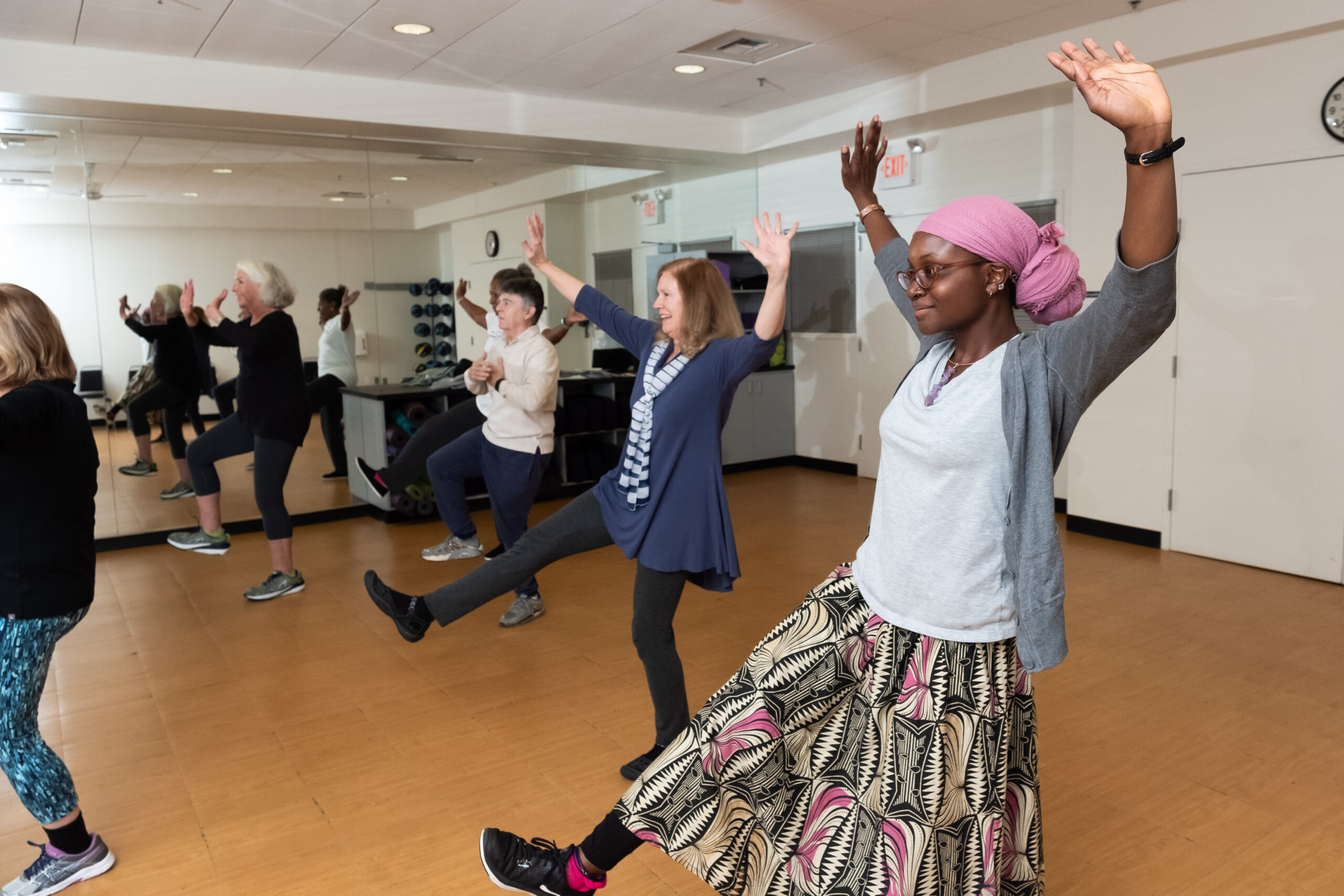 Group of adults in a fitness class raising arms and lifting legs in a studio.