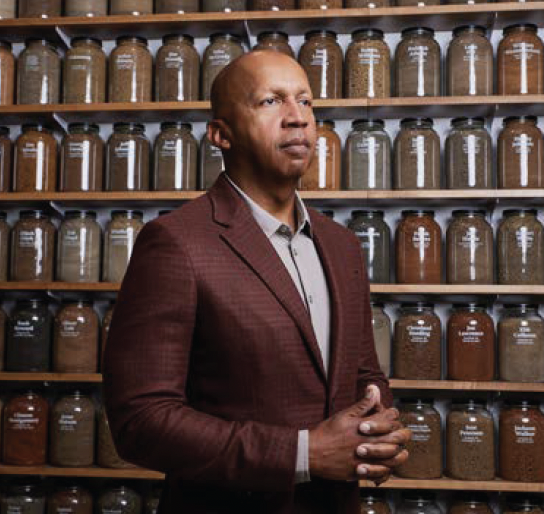 Portrait of Bryan Stevenson standing in front of shelves of labeled glass jars.