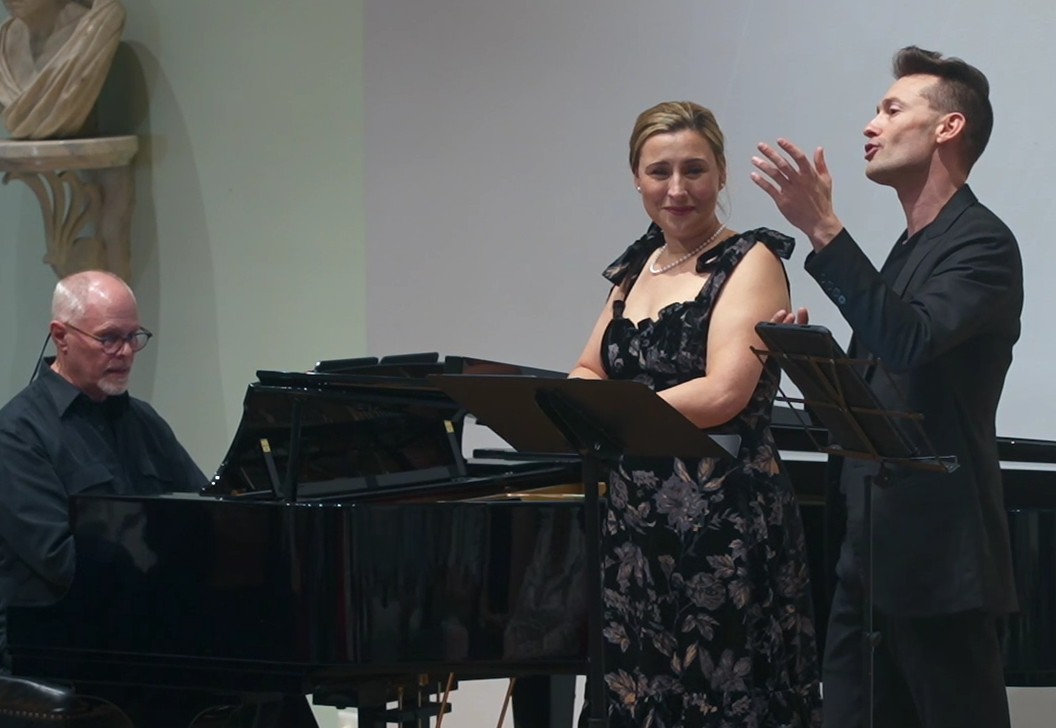 Three performers on stage, including a pianist and two vocalists, during a live concert.