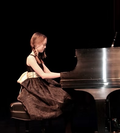 Young girl performing on piano on stage.