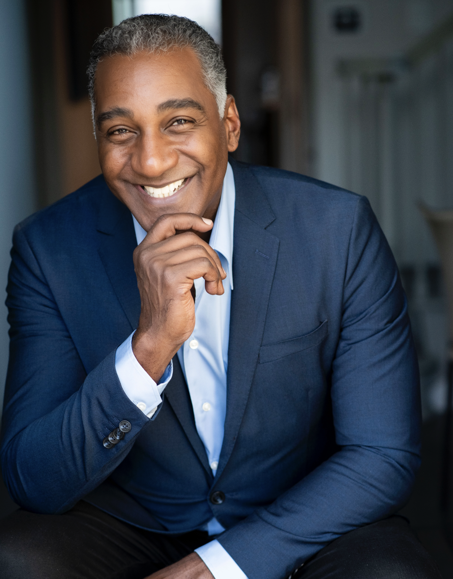 Portrait of a smiling man in a blue suit resting his chin on his hand.