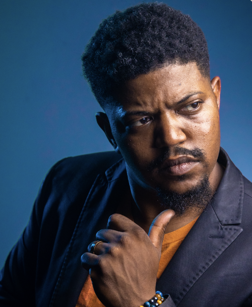Portrait of a man in a dark blazer looking thoughtfully to the side against a blue background.