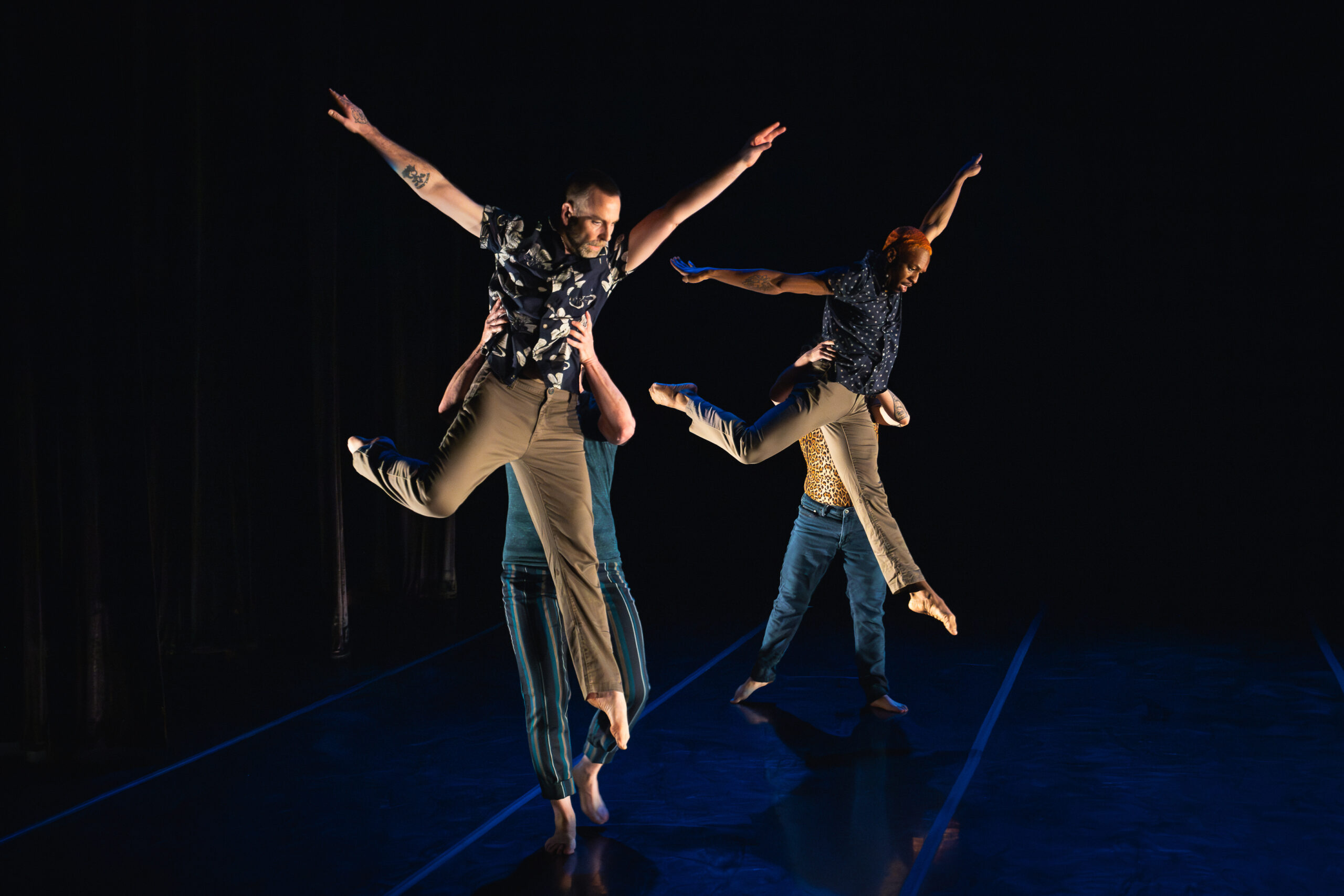 Two dancers are lifted by their partners during a contemporary dance performance on stage.