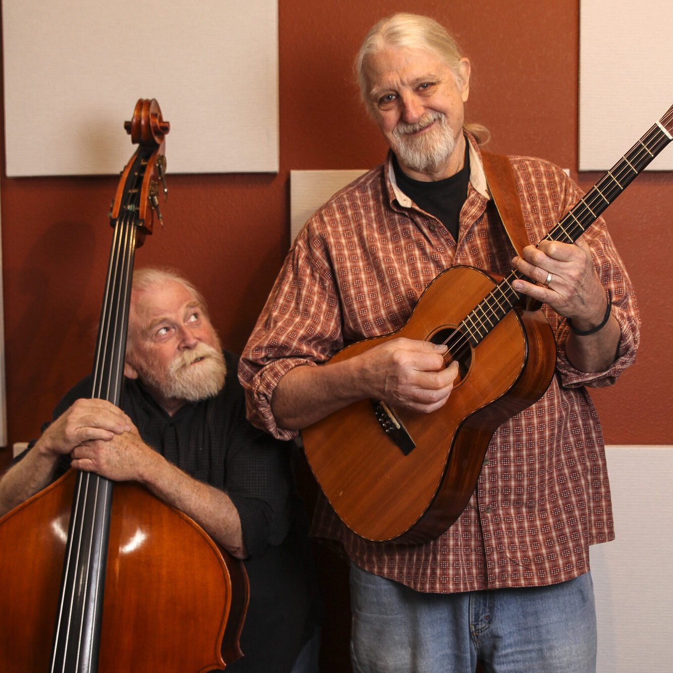 Two musicians pose with an acoustic guitar and an upright bass in a recording studio.