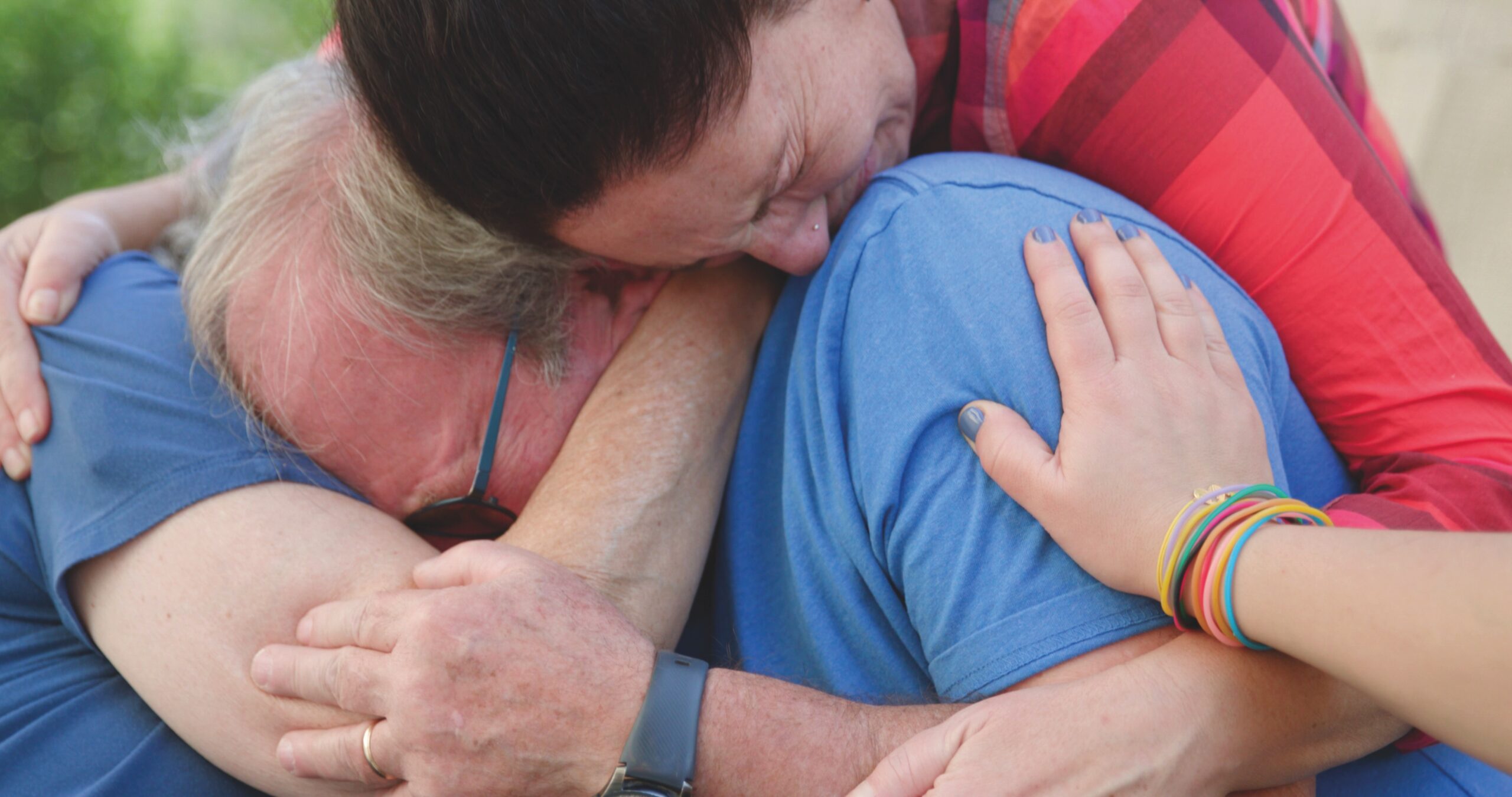 Three people share an emotional group hug outdoors.